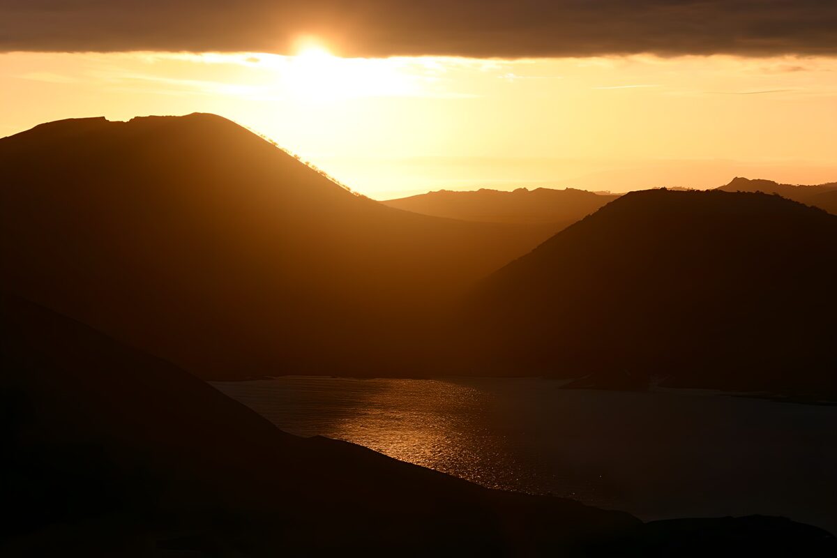 Sol bajo entre montañas y agua dorada