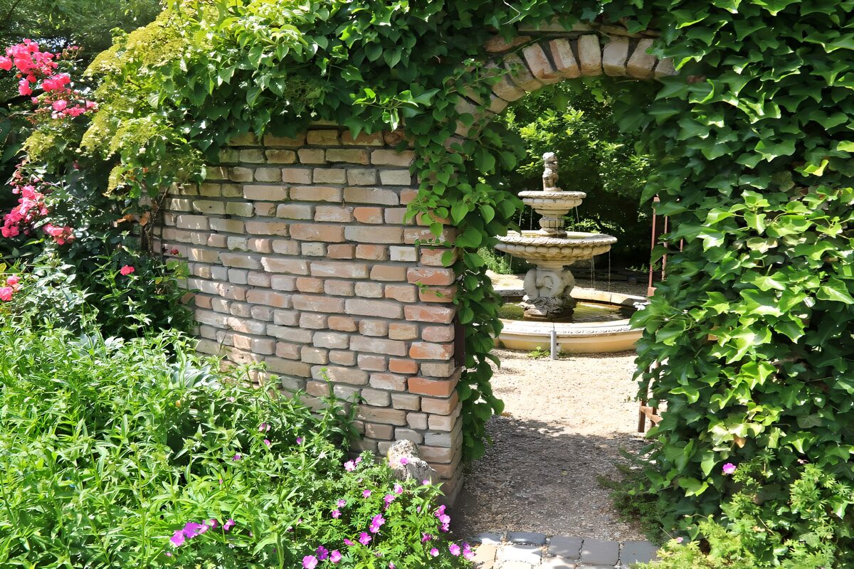 Fuente de jardín tras un arco de hiedra