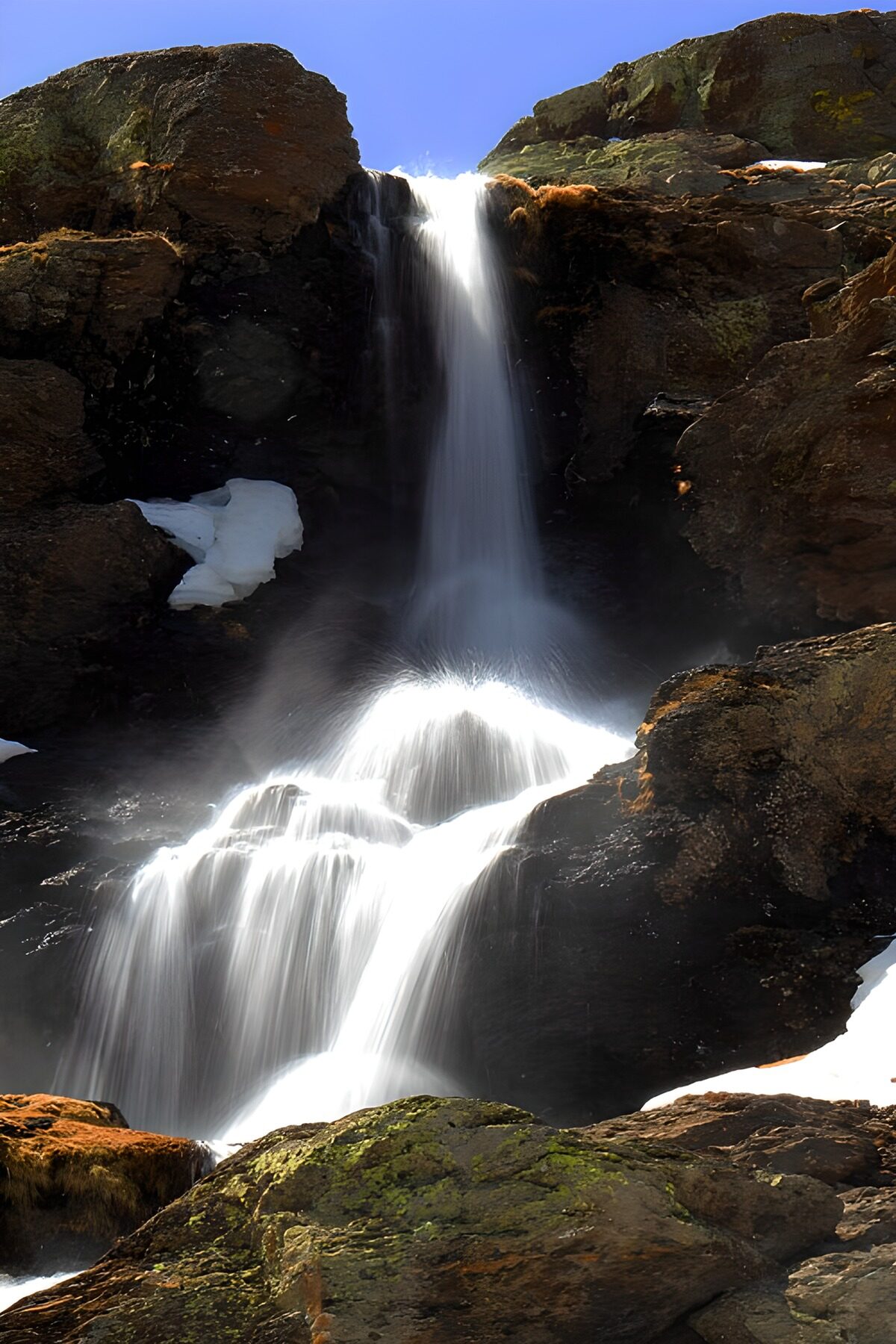 Cascada entre rocas oscuras y nieve