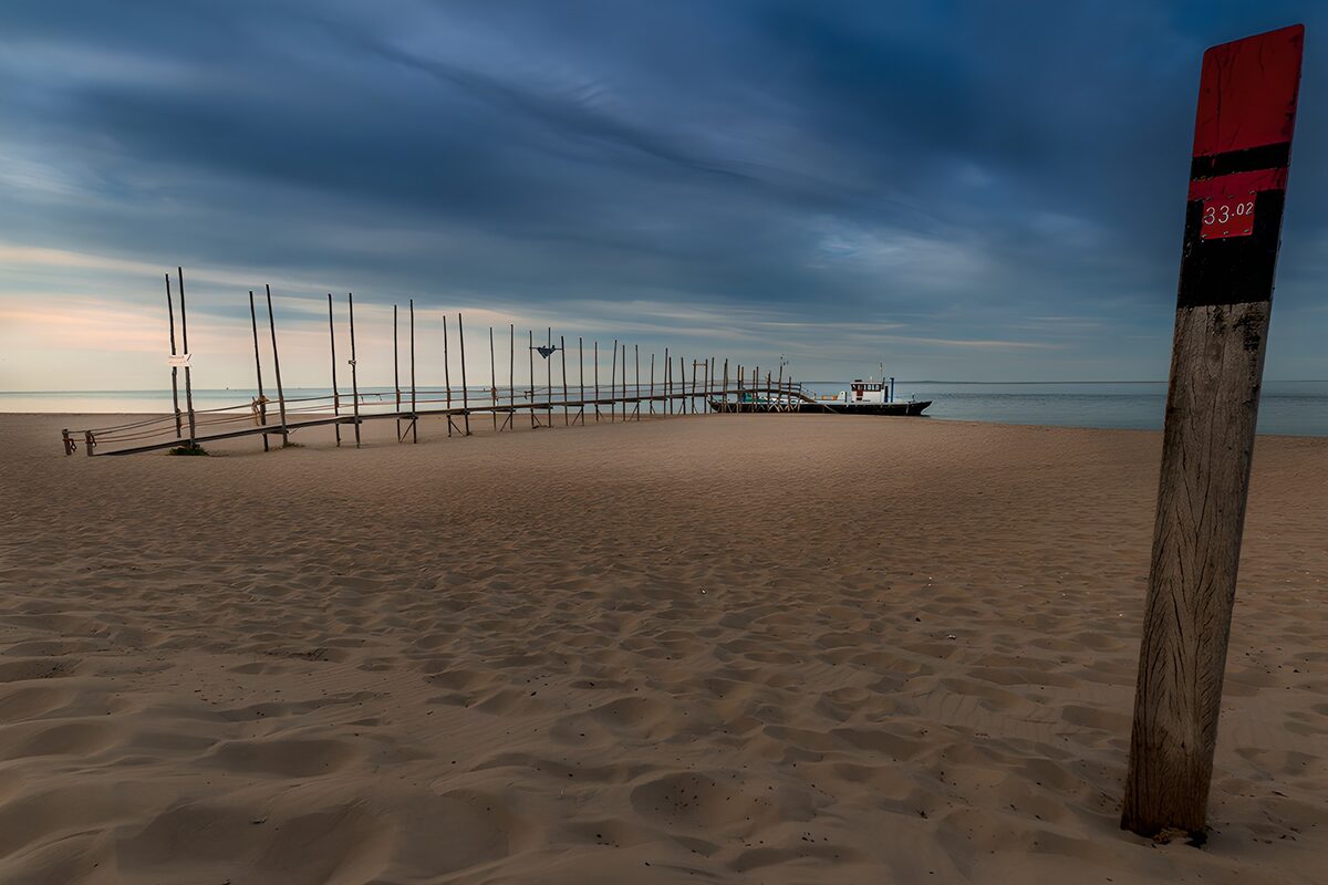 TPES76080: Playa con muelle bajo un cielo azul gris